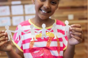 A young girl smiling while holding a paper chain of silhouettes 