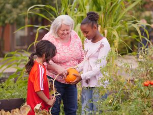 An elder and two children looking at pumpkins in a flourishing garden