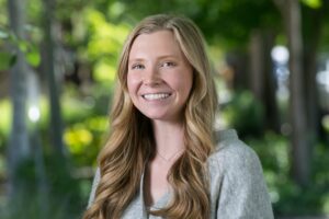 Headshot of Andrea Cornwell, Community Support Specialist for North Portland. She is a pale-skinned young woman with long, wavy blonde hair. She wears a grey sweater and a dainty necklace with a small row of pearls.