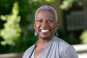 Headshot of Renee Moseley, a dark-skinned woman with very short grey hair and teardrop shaped, blue earrings.